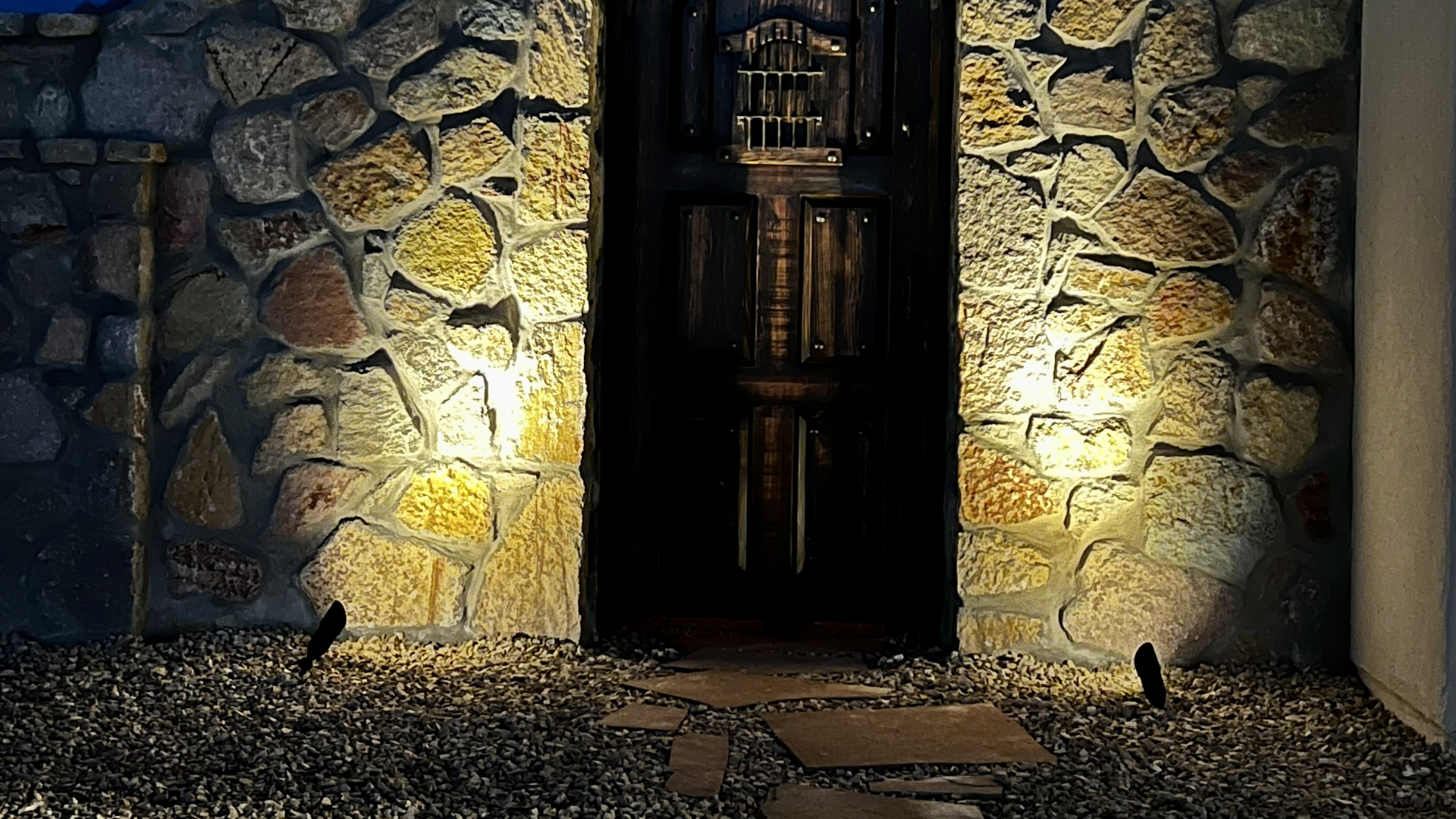 Spotlights shining on a stone wall around a rustic door on our client's property in Mesilla, NM. 