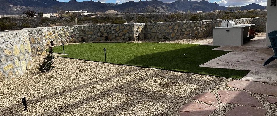 Green lawn in Alamogordo, NM, with landscaping rocks and a wall fence.