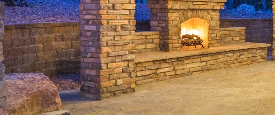 A wood-burning outdoor fireplace in Las Cruces, NM, on a stone patio near a rock landscape.